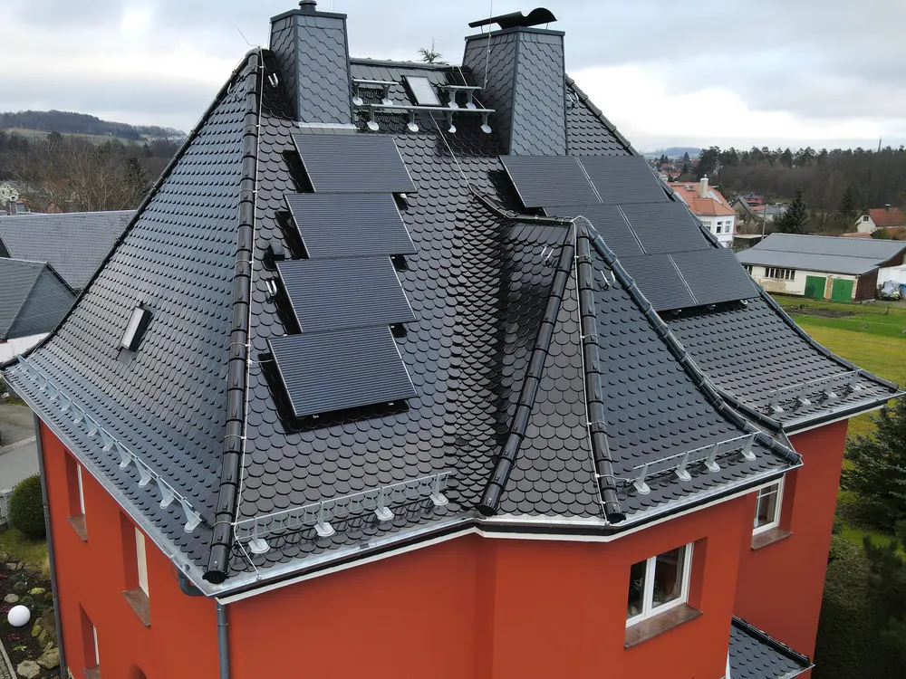 Rotes Haus mit schwarzem Ziegeldach, auf dem mehrere rechteckige Solarpaneele installiert sind.