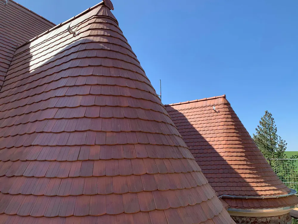 Zwei spitze, ziegelgedeckte Dächer eines Schlosses mit roten Ziegeln unter blauem Himmel.