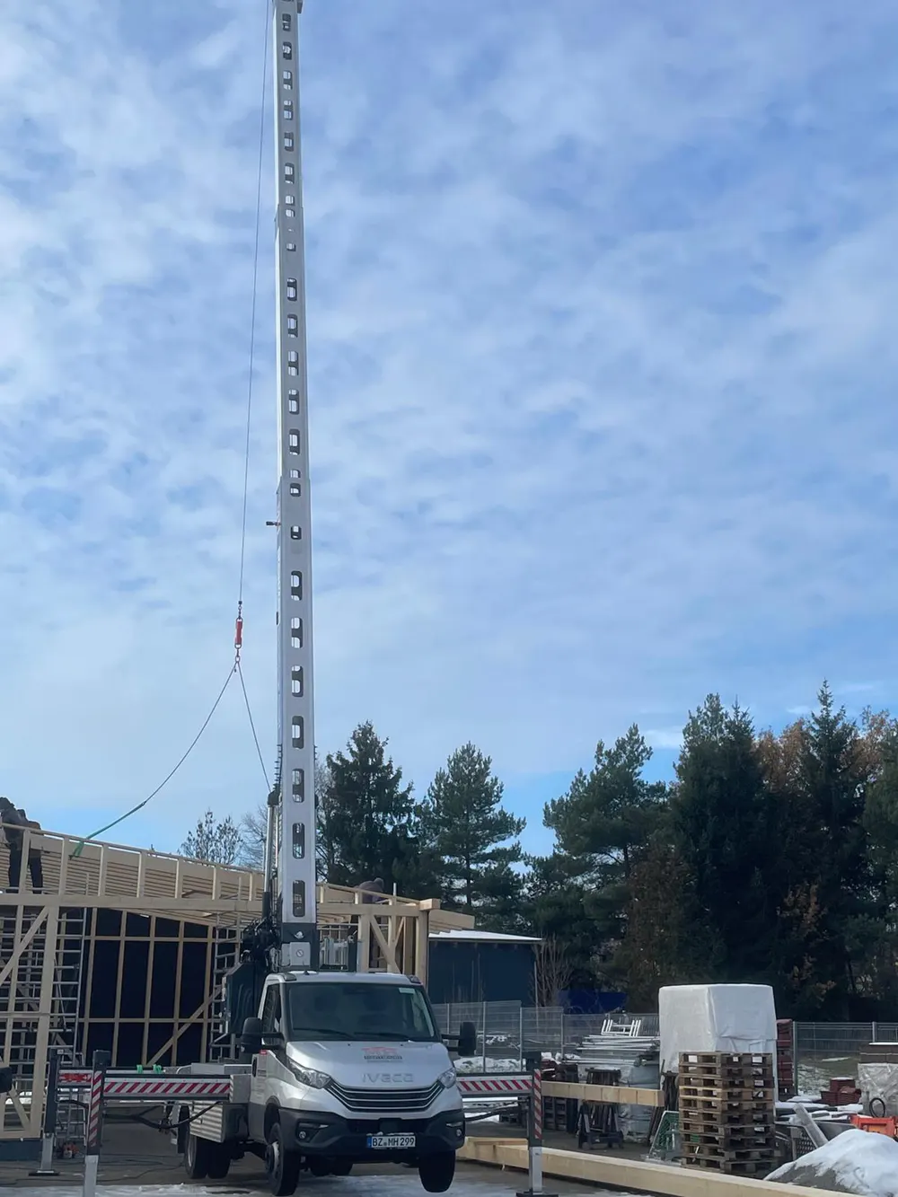 Ein LKW-Kran steht auf einer Baustelle, sein langer Ausleger ragt in den bewölkten Himmel.