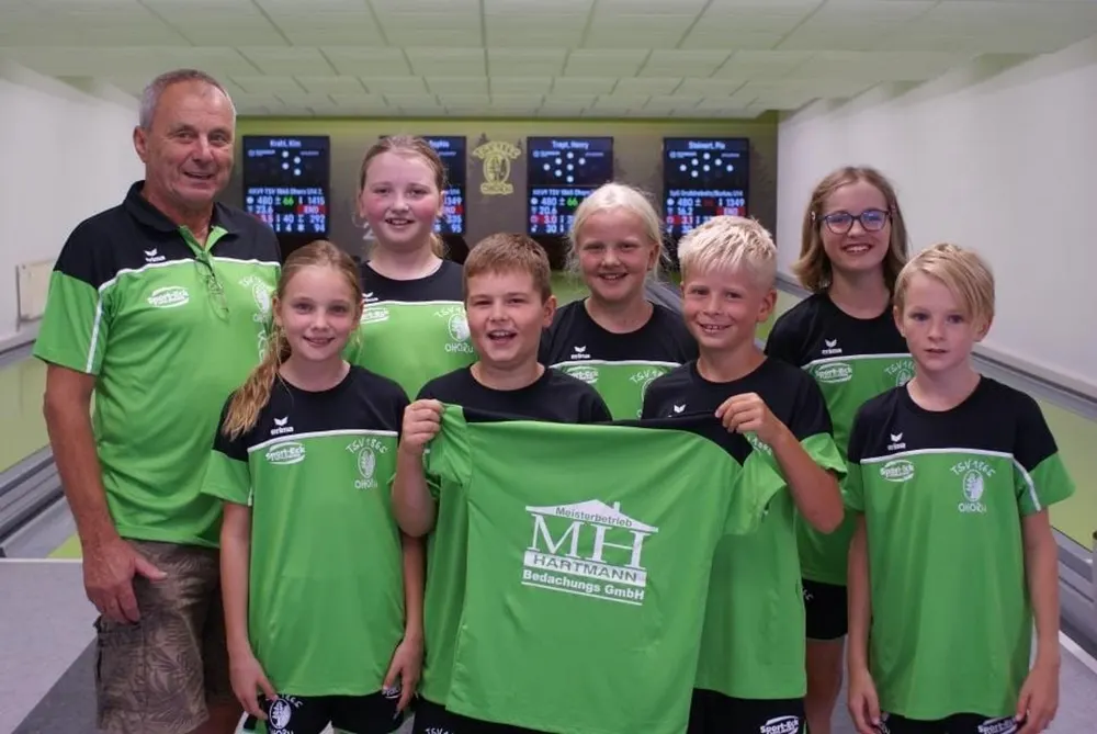 Ein Trainer und sieben junge Kegler in grünen Trikots, einer hält ein grünes T-Shirt mit dem Logo "MH Hantmann" hoch.