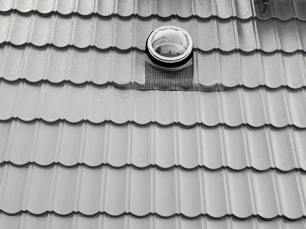 Dunkelgraues Wellblechdach mit einem runden Dachfenster.