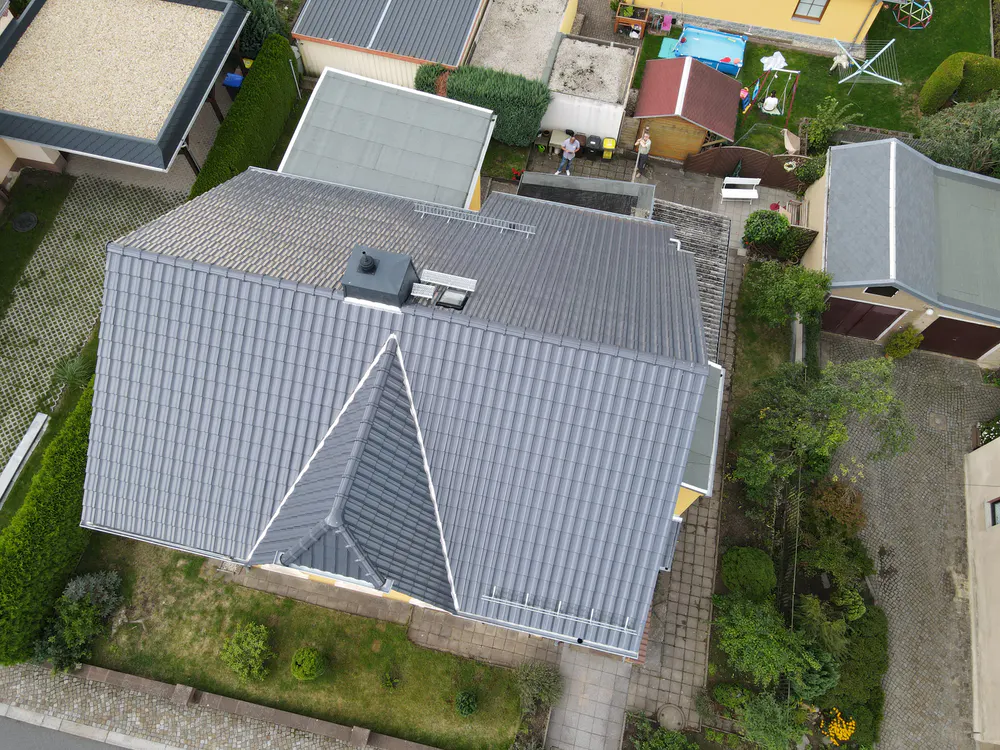 Draufsicht auf ein Einfamilienhaus mit neu gedecktem, dunkelgrauem Ziegeldach und Schornstein.