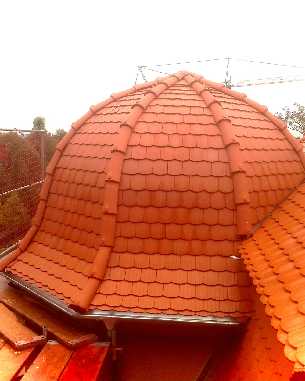 Rundes Dach mit orangefarbenen Dachziegeln und Dachrinne, im Hintergrund ein Baukran.