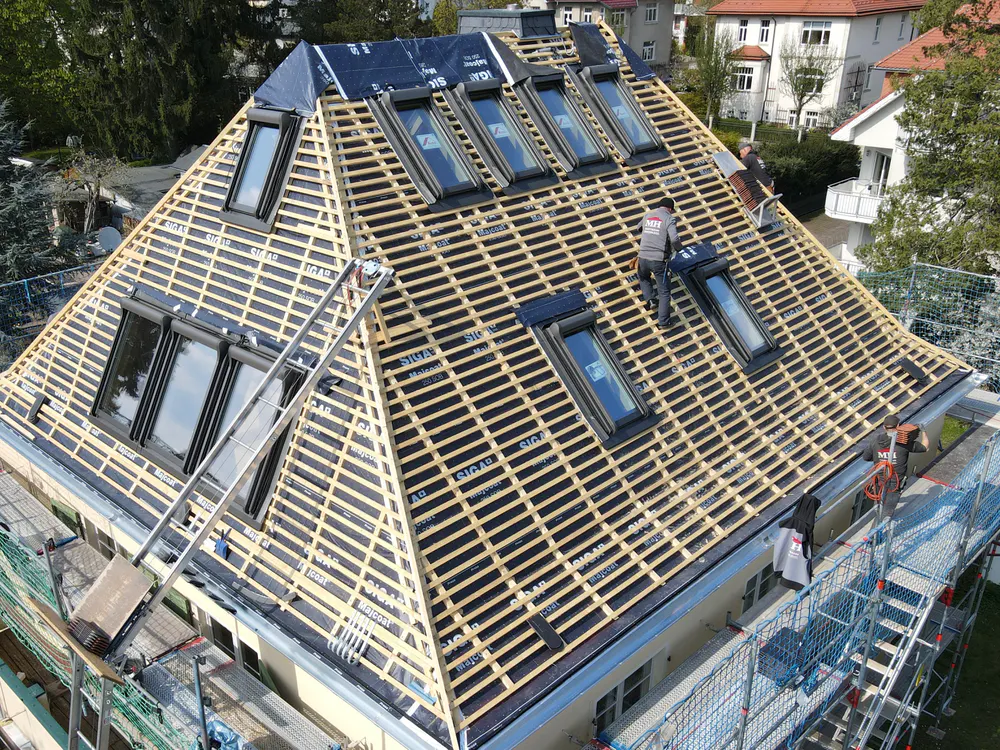 Dachdecker bei der Arbeit auf einem Dach mit Dachfenstern und Holzlatten.