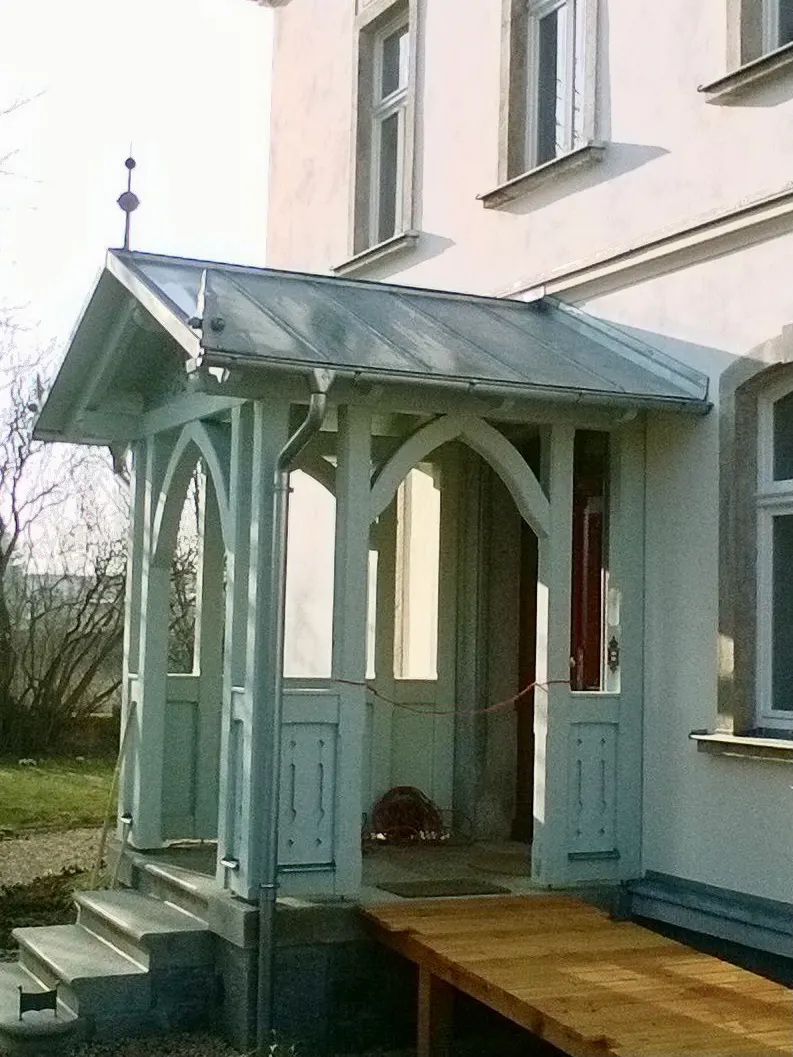 Ein weißes Haus mit einer Veranda, einer Holzrampe, Stufen und einem kleinen Vordach.
