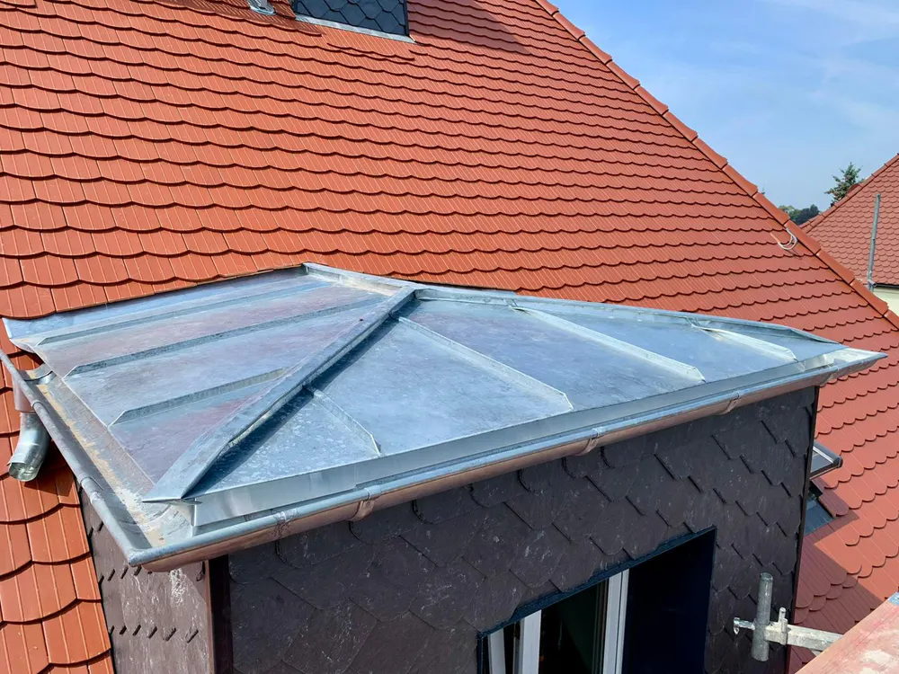 Dachgaube mit Zinkblechdach und Schieferverkleidung, rotes Ziegeldach im Hintergrund.