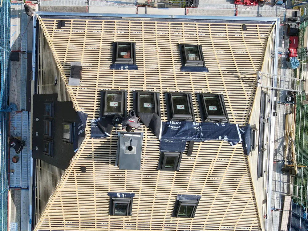 Draufsicht auf ein Dach in Bau mit Holzlattung, vielen Dachfenstern und einer Schornsteinöffnung.