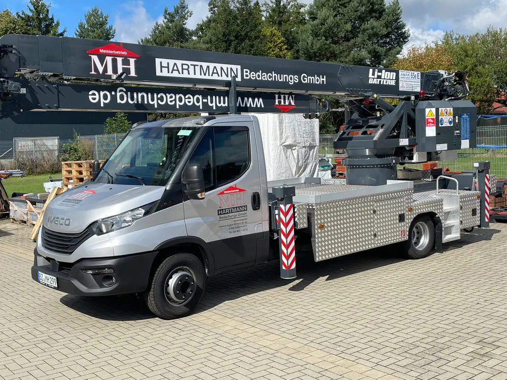 Silberner Iveco-Transporter mit MH Hartmann Bedachungs GmbH Logo und ausgefahrenem Kranarm mit "Li-Ion Batterie" Schriftzug.