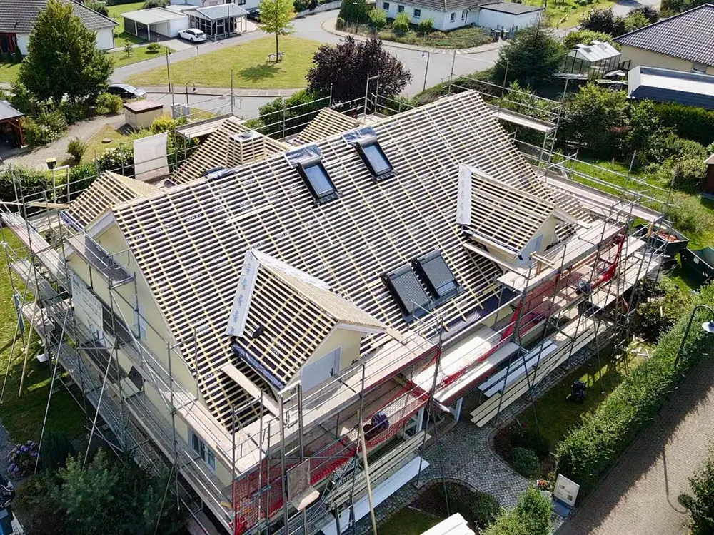 Drohnenansicht eines im Bau befindlichen Hauses mit neuem Dachstuhl, Dachfenstern und Gerüst.