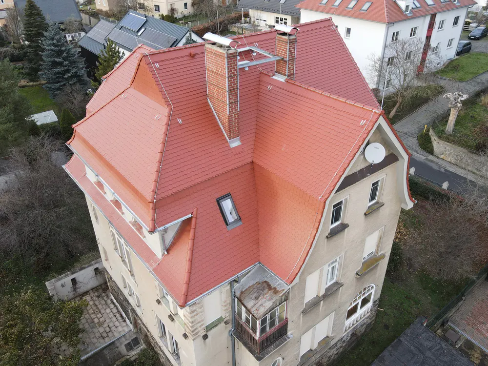 Dach eines Mehrfamilienhauses mit roten Ziegeln und Schornstein, von oben gesehen.