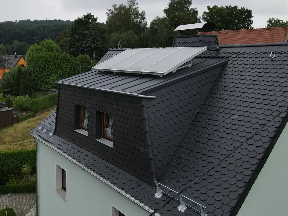 Dach eines weißen Hauses mit dunklen Schindeln und Solarpaneelen.