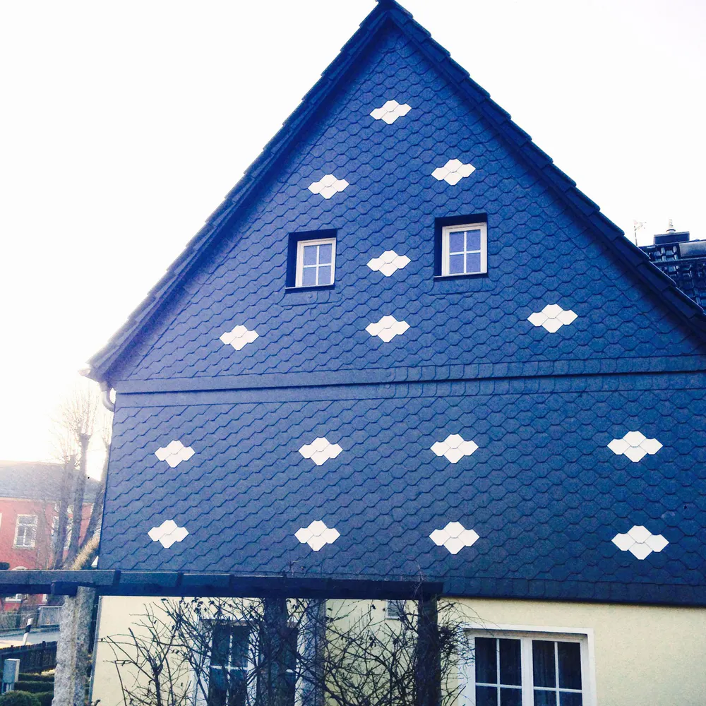 Blaues Schieferhaus mit weißen Wolkenmustern und zwei kleinen Fenstern im Giebel.
