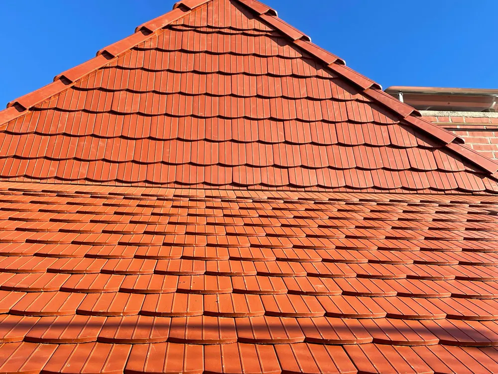 Rotes Ziegeldach eines Hauses mit Giebel vor blauem Himmel.