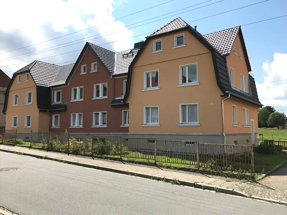 Reihe von drei Wohnhäusern mit orangefarbenen, braunen und gelben Fassaden unter blauem Himmel.