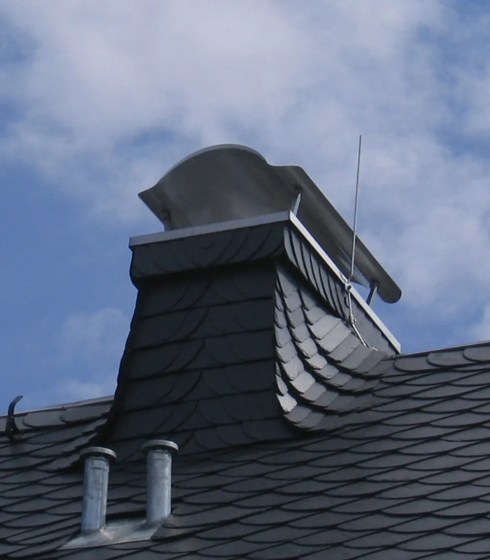 Dach mit Schieferziegeln, Schornstein mit Metallabdeckung und zwei Metallentlüftungsrohren.