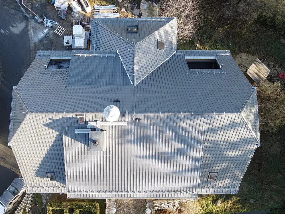 Dach eines Hauses mit grauen Ziegeln, Dachfenstern und Satellitenschüssel, Baumschatten.