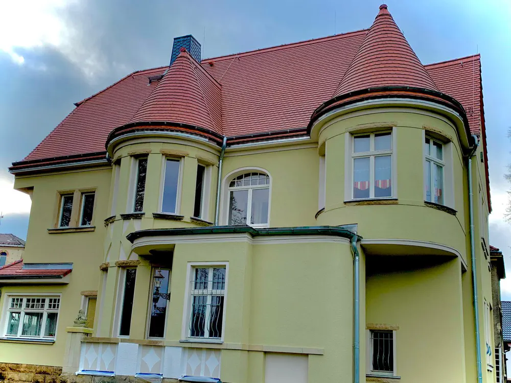 Gelbe Villa mit rotem Ziegeldach, zwei runden Türmen und vielen Fenstern.
