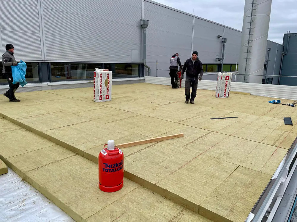 Dachdecker arbeiten auf einem Flachdach, das mit Dämmplatten ausgelegt ist, mit einem roten Gastank im Vordergrund.