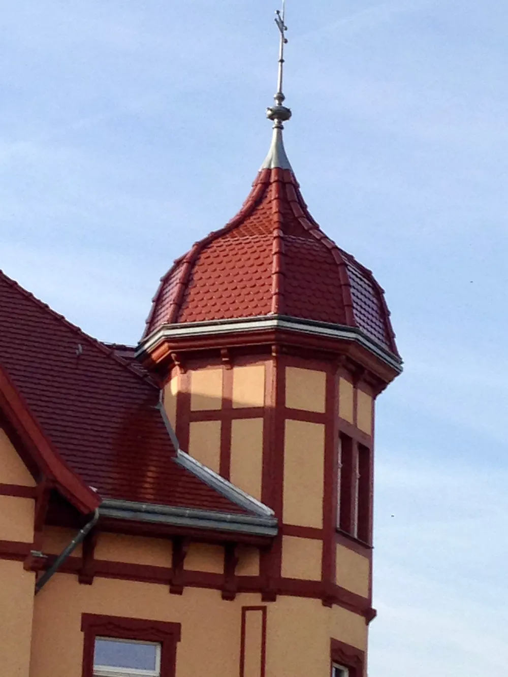 Turm einer Kirche oder eines Hauses mit rotem Dach, gelben Wänden und einem Kreuz auf der Spitze.