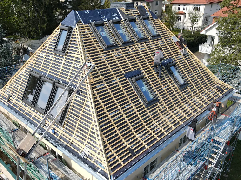 Dachdecker verlegen Dachlatten auf einem Spitzdach mit vielen Dachfenstern und Unterspannbahn.