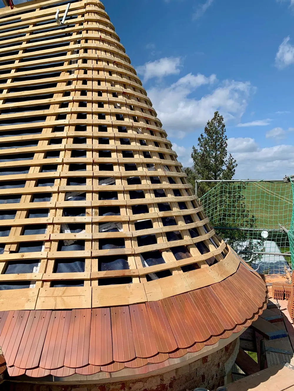 Konisches Dach mit Holzlatten und Dachziegeln im Bau unter blauem Himmel.