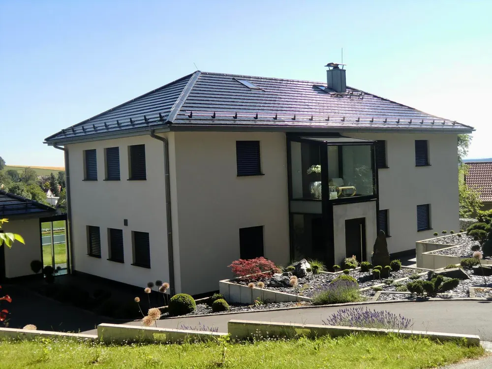 Modernes Einfamilienhaus mit heller Fassade, dunklem Dach, großem Wintergarten und angelegtem Steingarten.