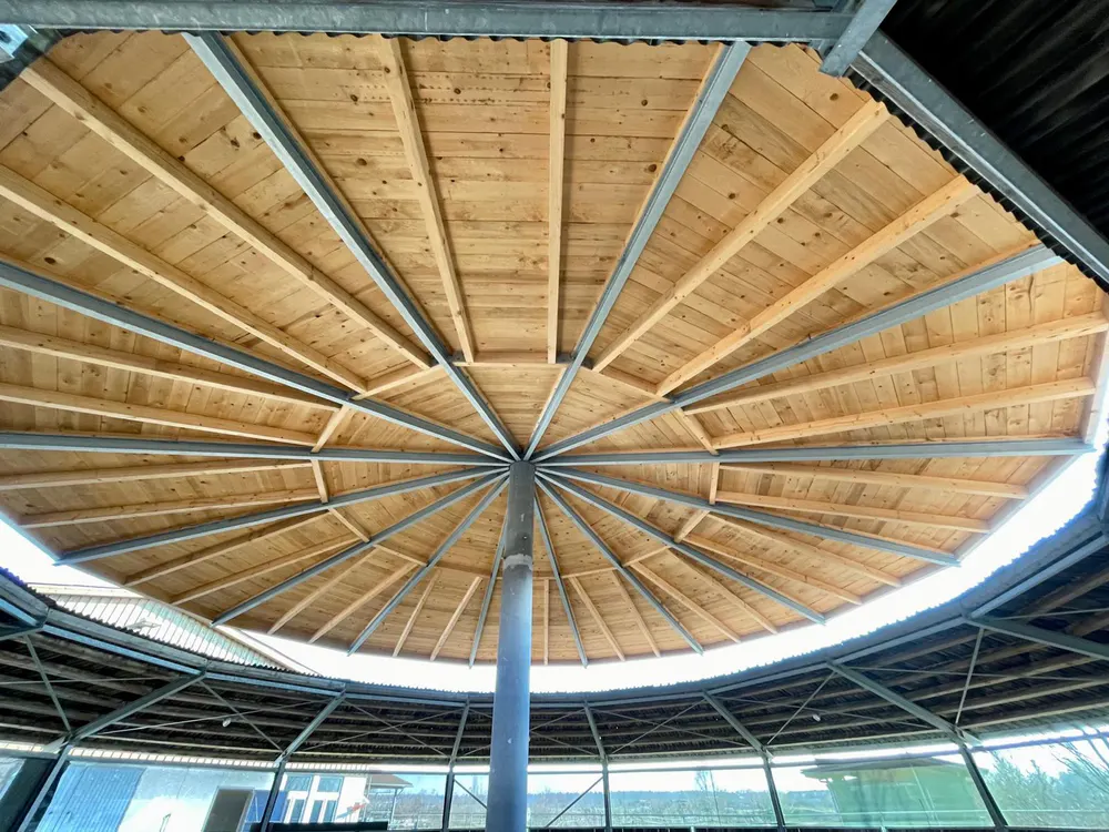 Rundes Holz- und Metallvordach von unten gesehen, mit zentraler Stützsäule und radialen Balken.