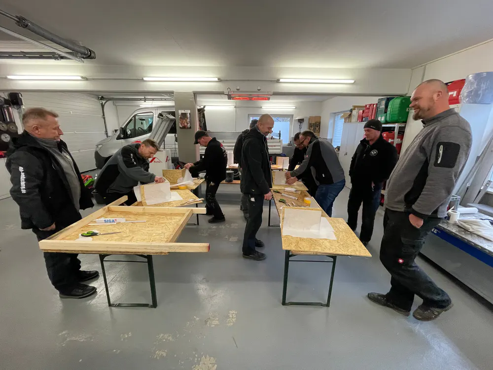 Männer in einer Garage arbeiten an Holztischen mit Werkzeugen und Plänen.