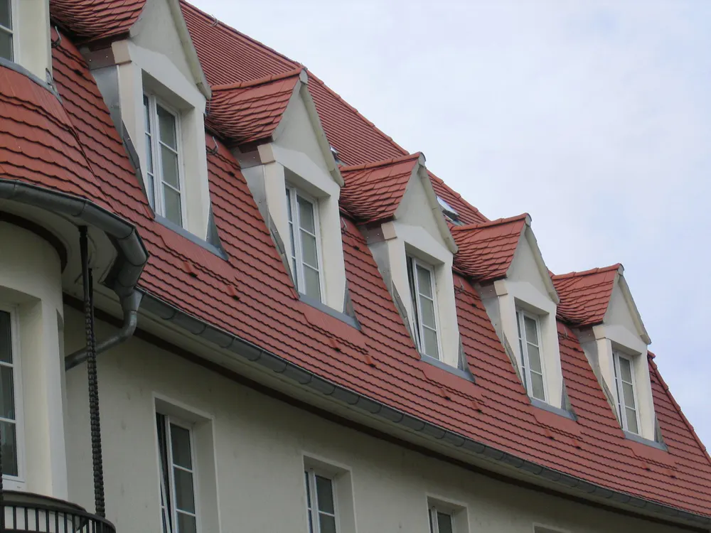 Ziegeldach mit fünf Gaubenfenstern an einem hellen Gebäude.