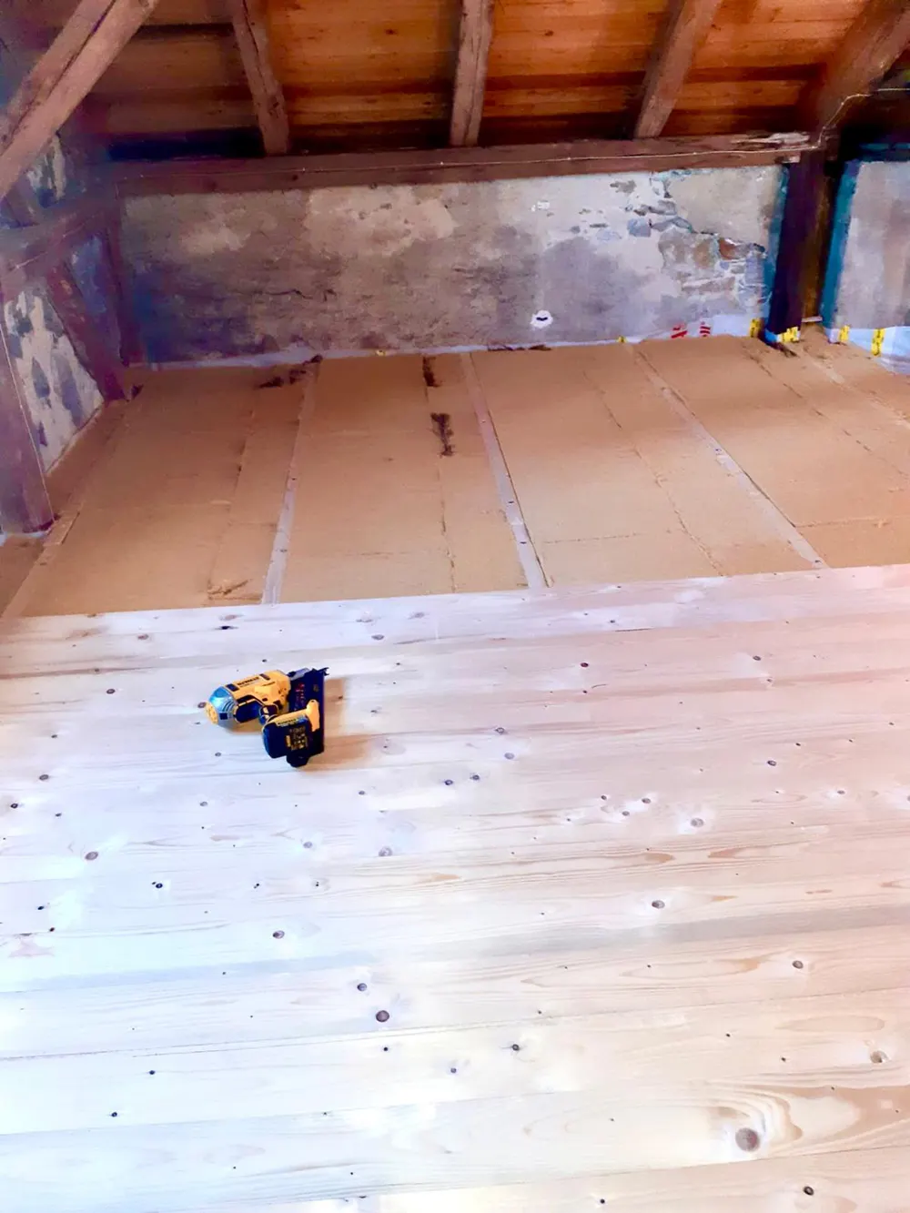 Dachboden mit Holzbalken, weiß lasiertem Holzboden und einer gelben Nagelpistole.