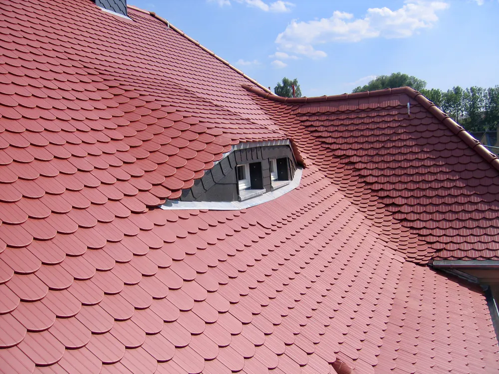 Rotes Ziegeldach mit einer Gaube und drei kleinen Fenstern unter einem blauen Himmel.