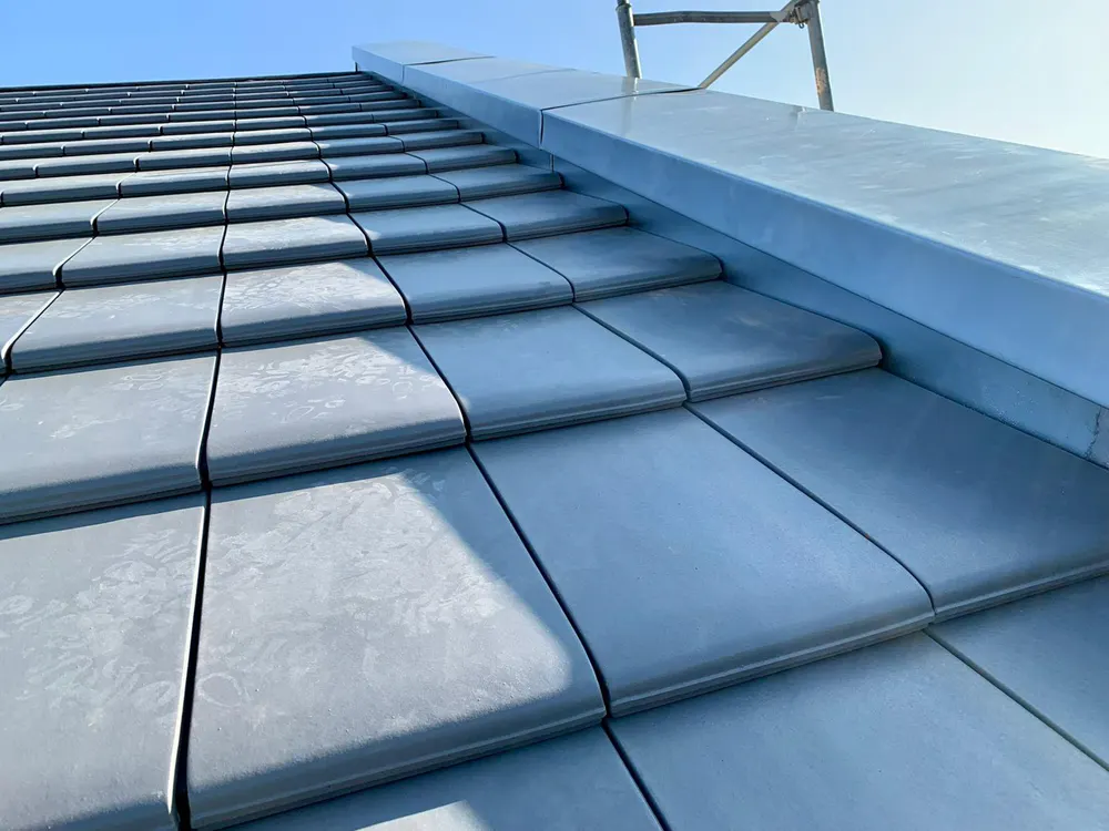 Graue Dachziegel und ein graues Blechdach auf einem Haus unter blauem Himmel.