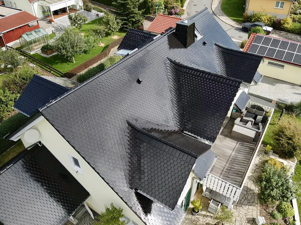 Dach eines Hauses mit glänzenden, schwarzen Ziegeln und einem Holzbalkon.